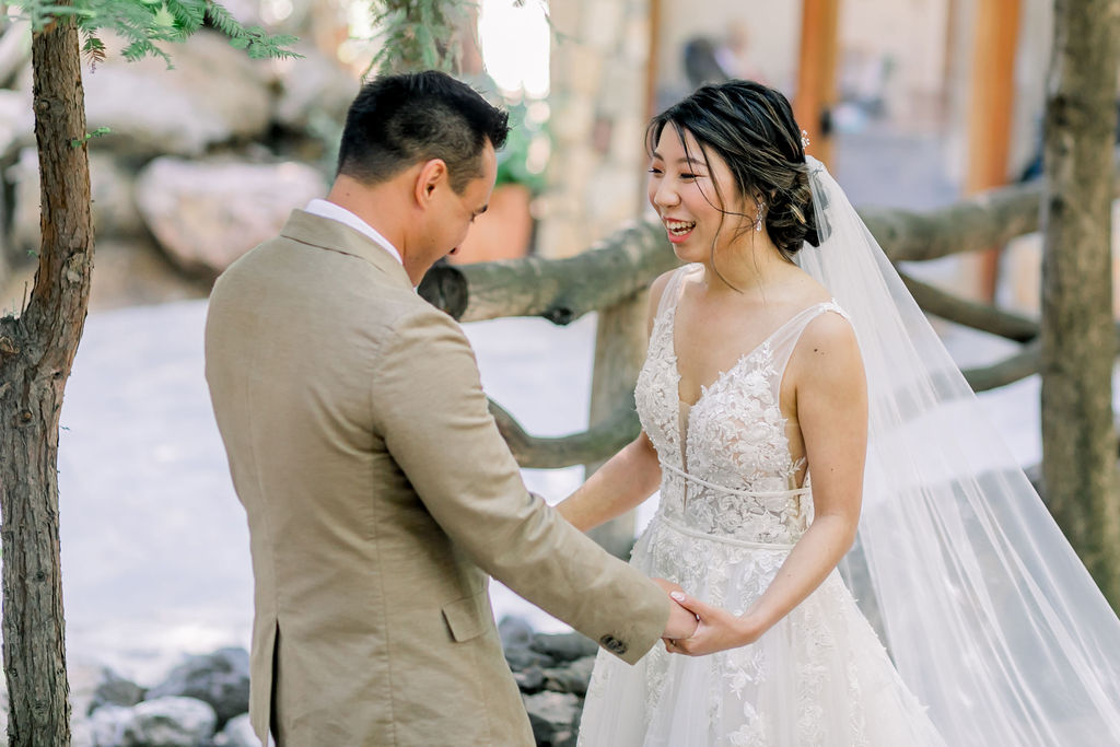 An enchanting wedding at Calamigos Ranch, groom in tan suit with floral tie has first look with bride wearing a floral lace appliqué deep v-neck wedding dress