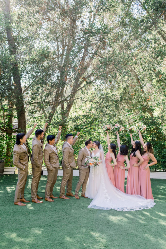 groom and bride with wedding party wearing tan suits with floral ties and coral pink bridesmaid dresses