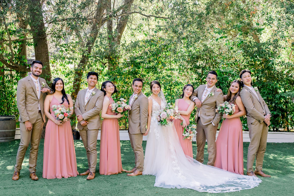 groom and bride with wedding party wearing tan suits with floral ties and coral pink bridesmaid dresses