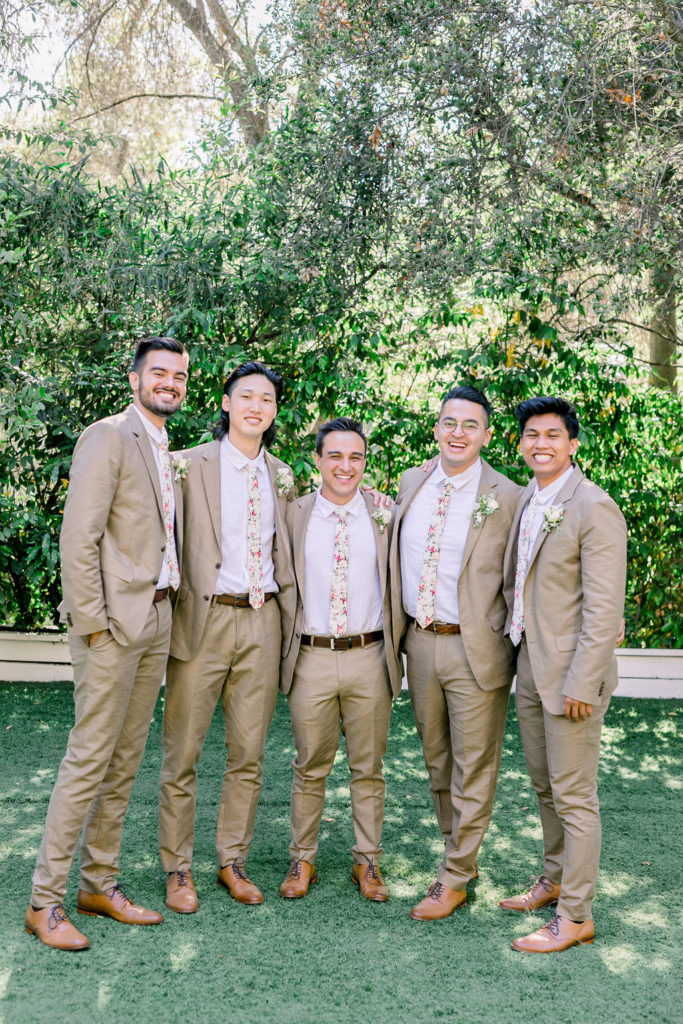 groom standing with groomsmen wearing tan suits and floral ties