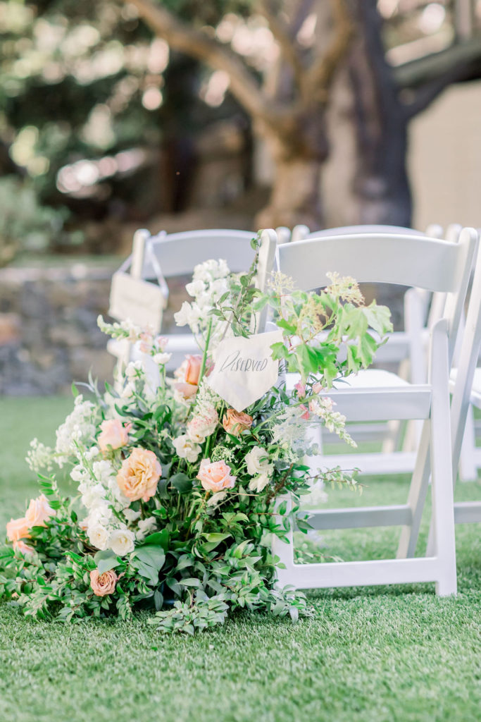 white ceremony chairs with large floral arrangement in aisle and white reserved sign