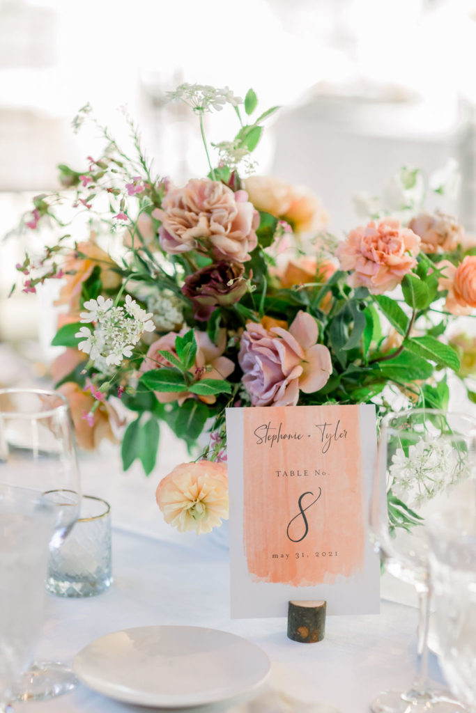 wedding reception tables at the Redwood Room at Calamigos Ranch with pink and orange floral centerpieces and orange watercolored table numbers