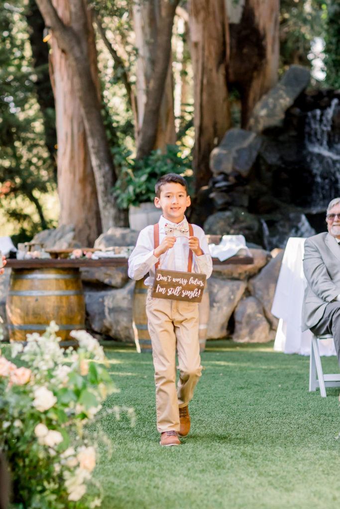 ring bearer wearing khakis and pink suspenders holds a sign that says "don't worry ladies, I'm still single"