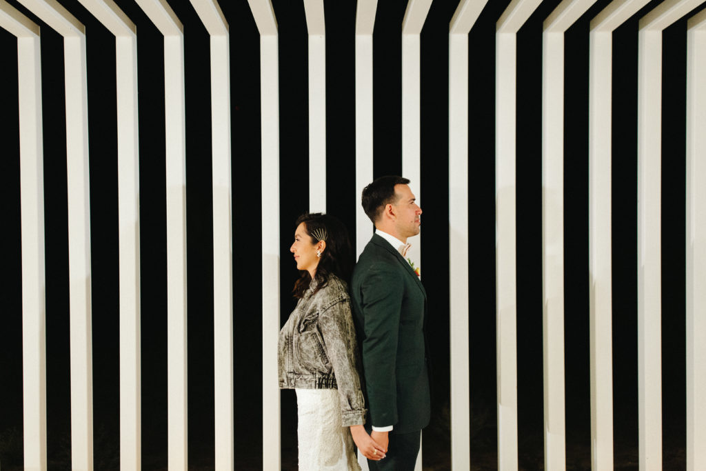 bride and groom hold hands in front of striped wall during wedding reception