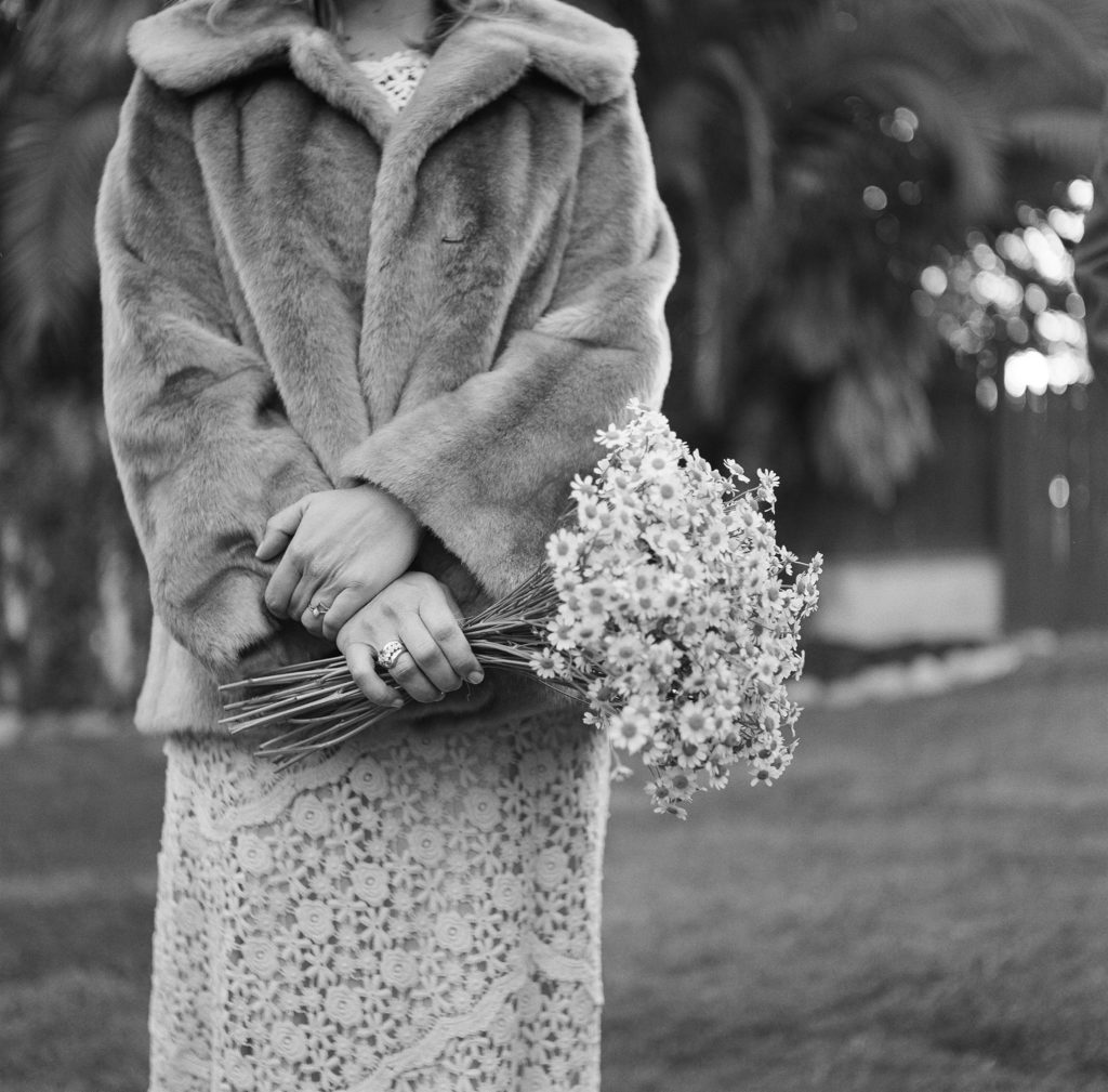 bride in fur coat and daisy bouquet with groom in maroon suit take portrait shots