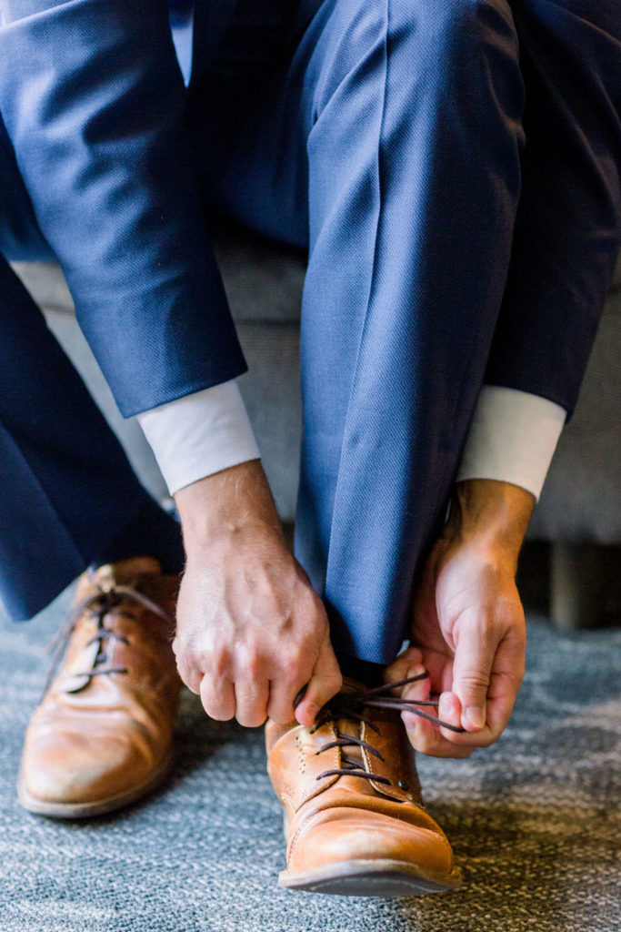 groom tying brown shoes before wedding