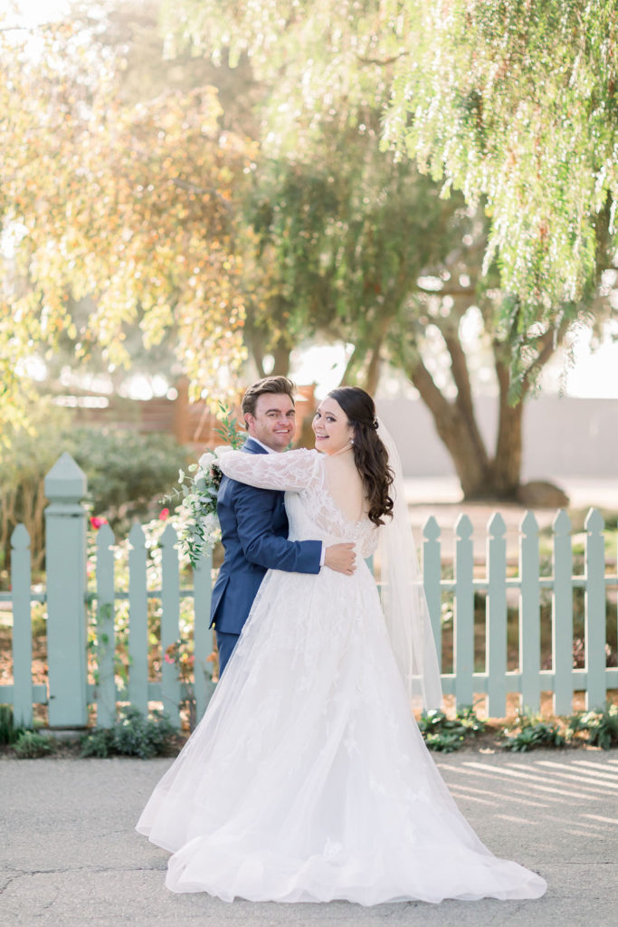 bride in long sleeve wedding dress with groom in blue suit take portrait shots at sunset