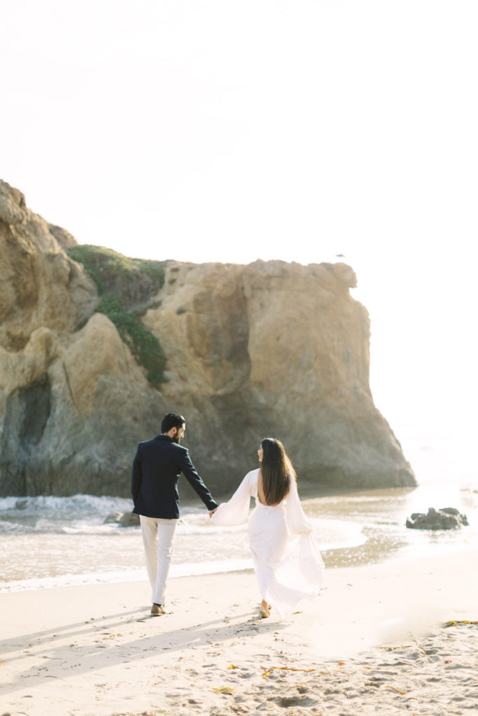 couple walks towards sunset during beach engagement photoshoot