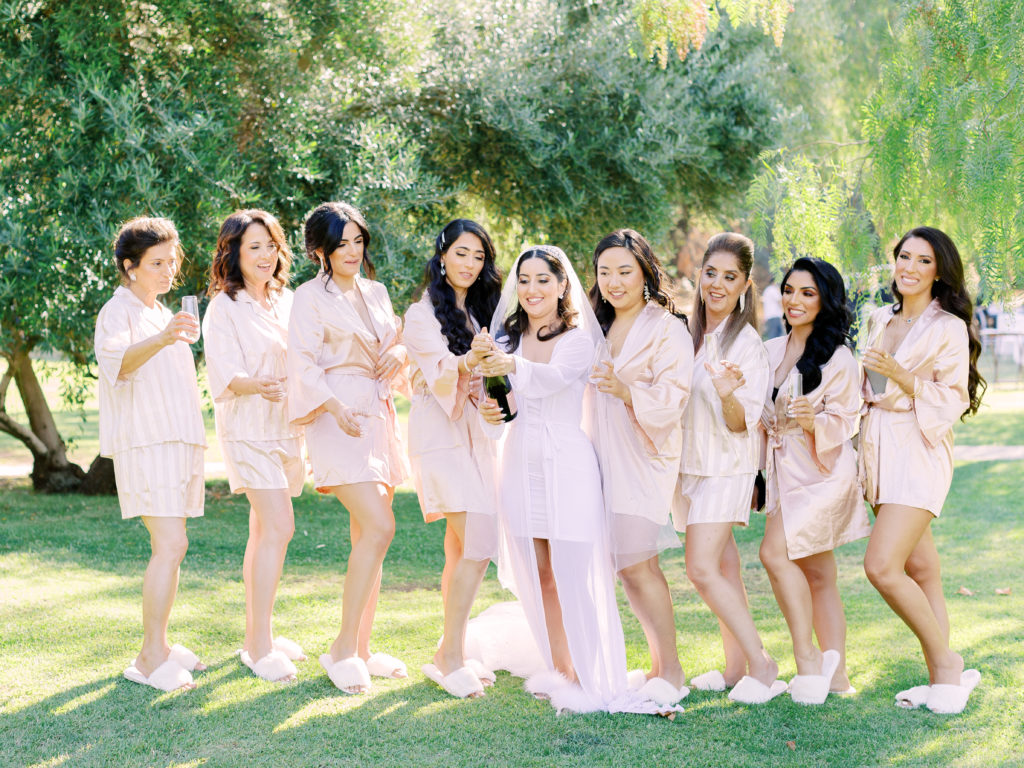 bride opens champagne with bridesmaids in robes