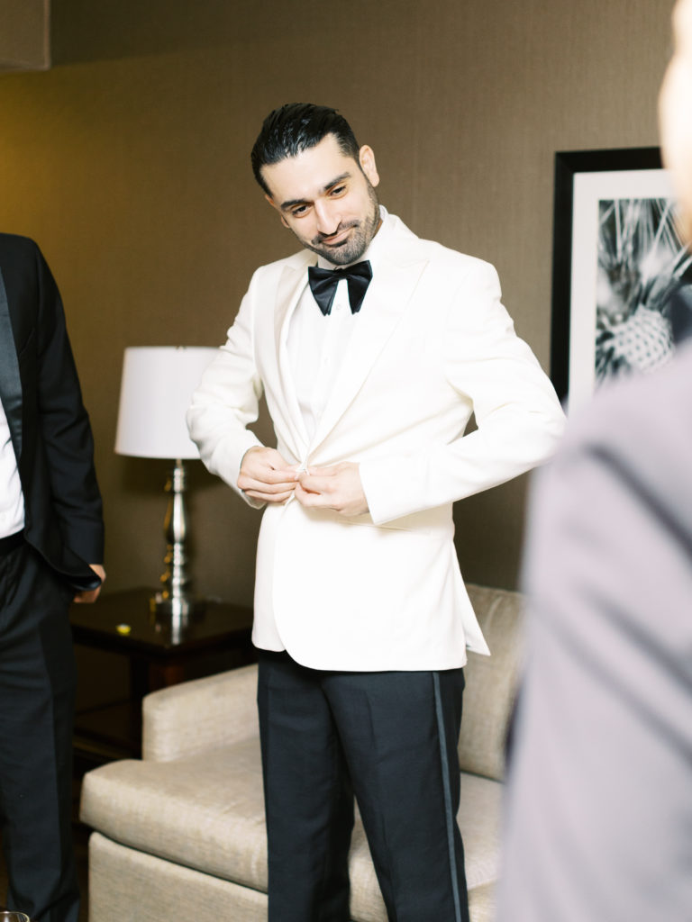 groom in white tuxedo and black bowtie gets ready for wedding