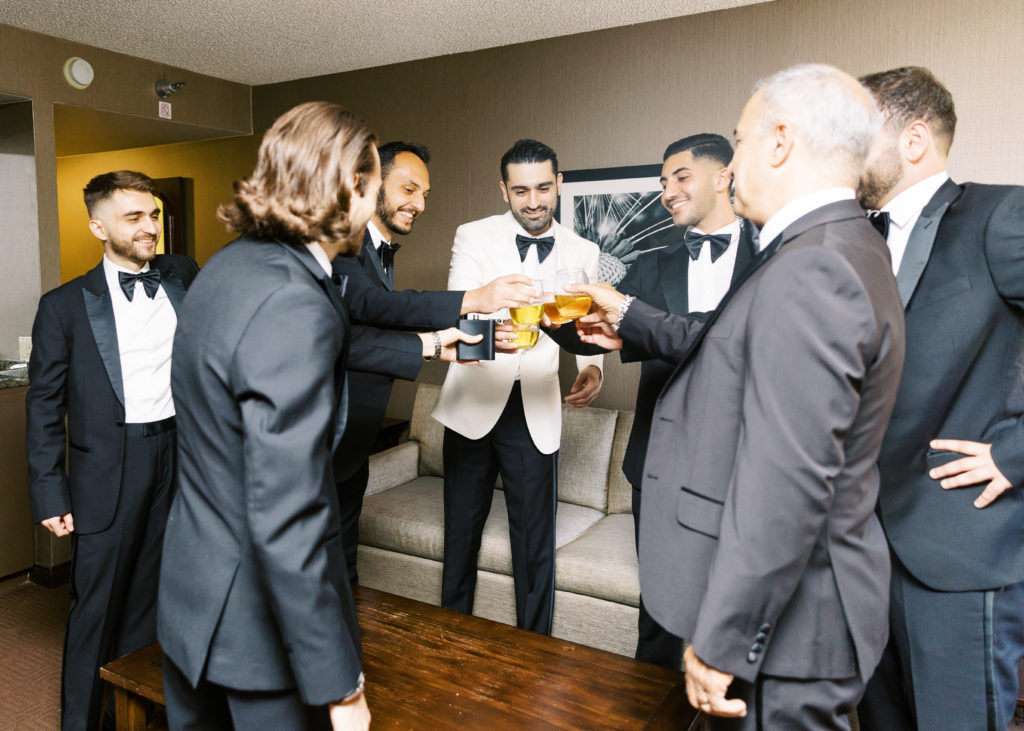 groom in white tuxedo and black bowtie gets ready for wedding with groomsmen