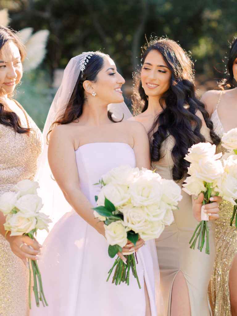bride in strapless ballgown with bridesmaids in mix matched gold dresses holding white rose bouquets