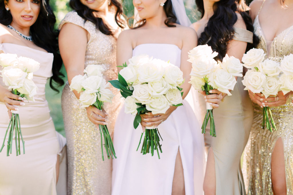 bride in strapless ballgown with bridesmaids in mix matched gold dresses holding white rose bouquets