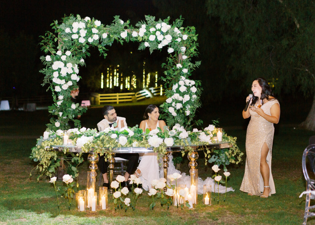 bride and groom sit at sweetheart table during wedding reception while listening to speeches