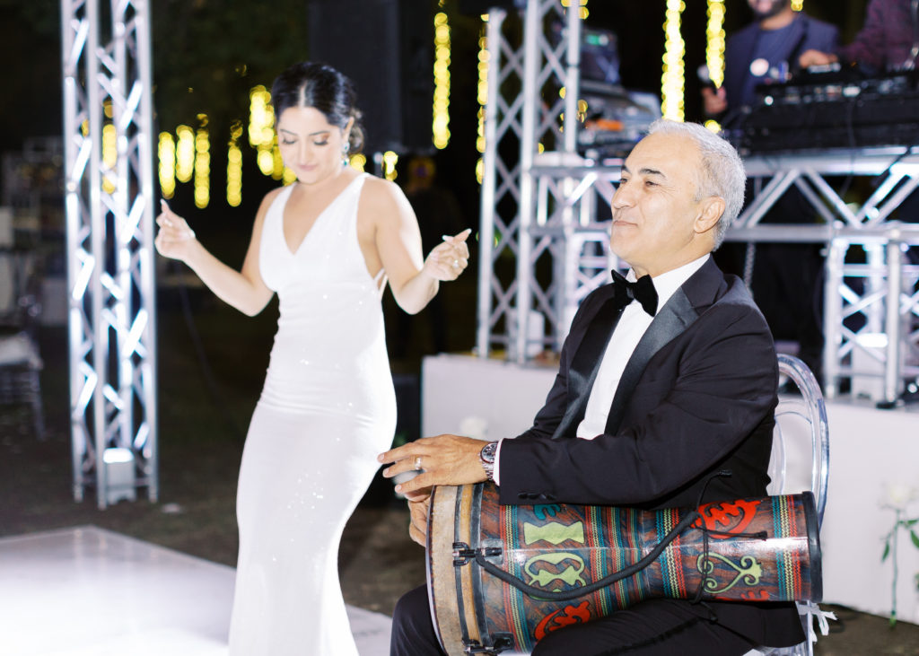 bride in reception dress dances while father of the bride plays instrument