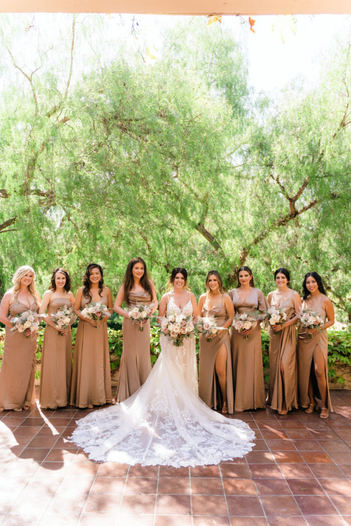 bride in floral appliqué dress stands with bridesmaids in beige satin dresses