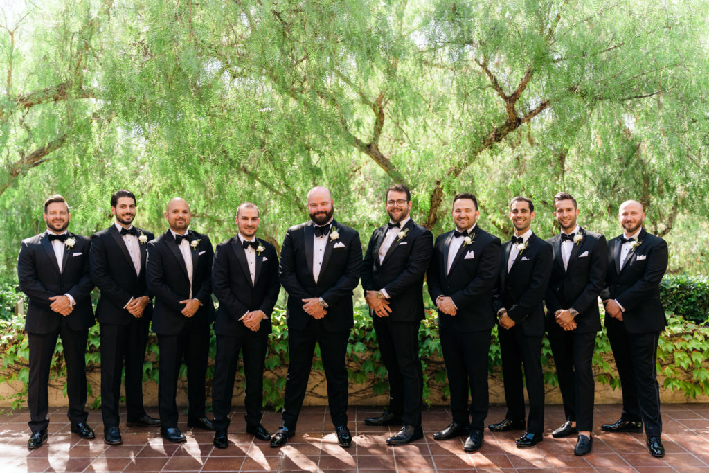 groom stands with groomsmen in black tuxedo suits
