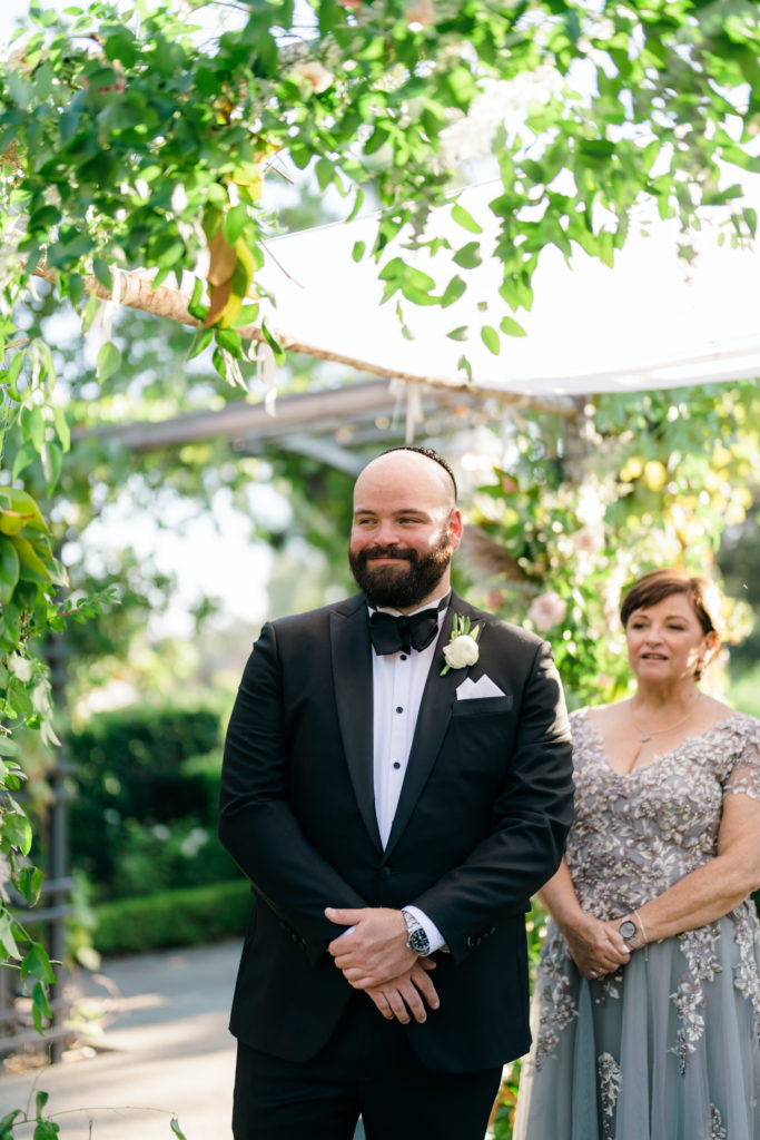 Groom in black tuxedo suit stands at wedding ceremony altar