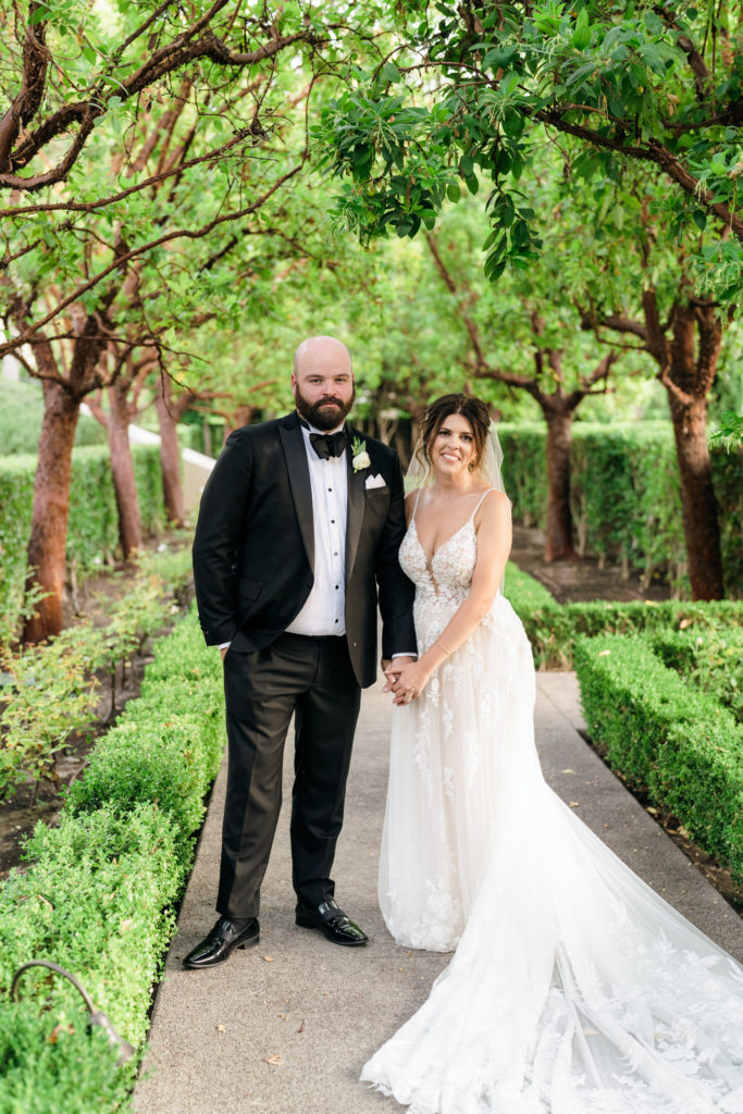 bride and groom walk together on tree line garden path