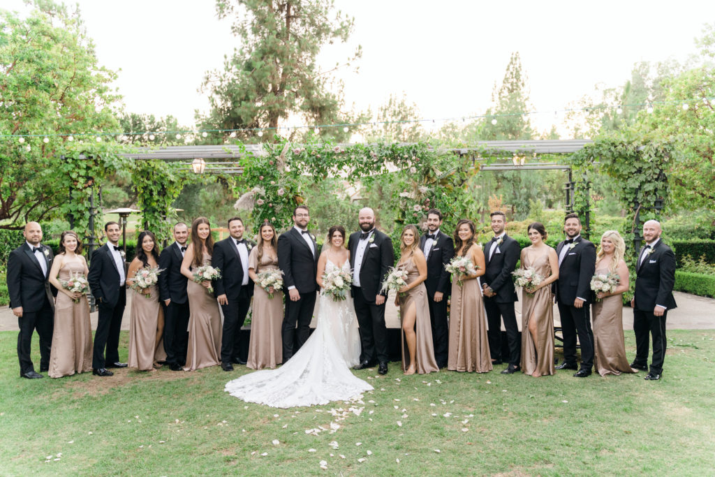 bride and groom stand with wedding party in beige satin dresses