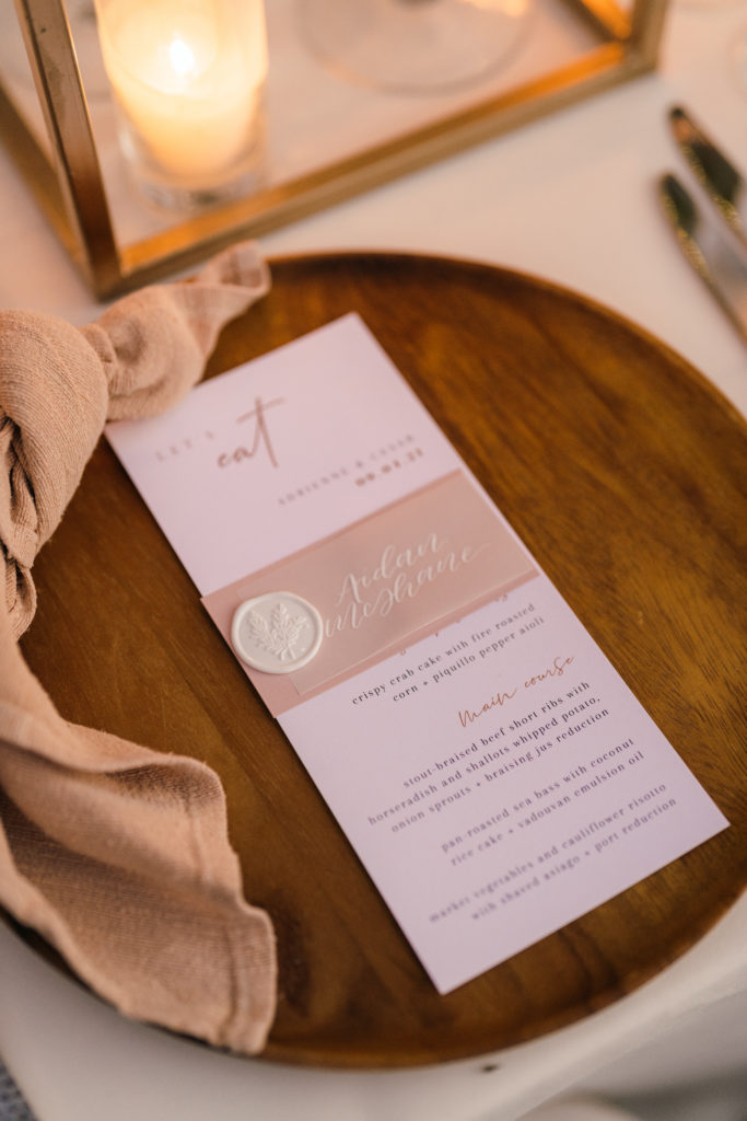 wedding reception menu with wax seal on top of wooden plate charger and beige linen napkin