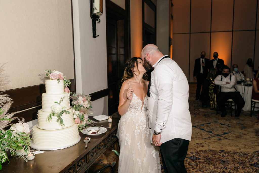 bride in floral appliqué dress kisses groom during cake cutting
