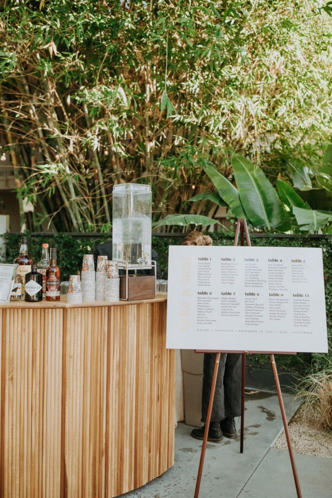 mid-century inspired wooden bamboo dowel bar with welcome beverages next to a seating chart