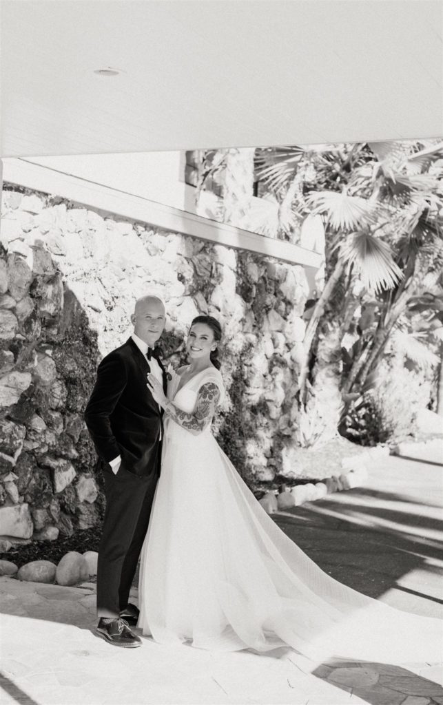 bride in modern asymmetrical dress stands with groom in maroon velvet suit jack in front of the Capri Hotel in Ojai