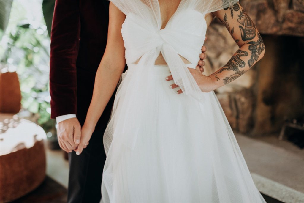 bride in modern asymmetrical dress stands with groom in maroon velvet suit jacket in the Capri Hotel in Ojai