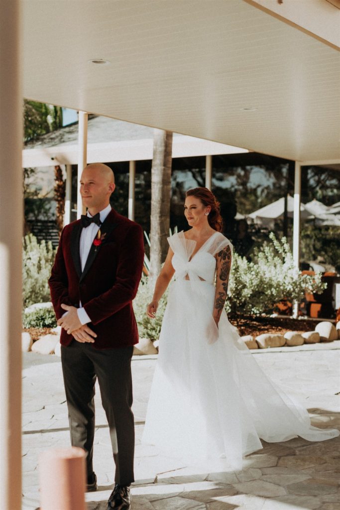 groom in maroon velvet suit jacket waits for first look with bride in modern asymmetrical dress at the Capri Hotel in Ojai