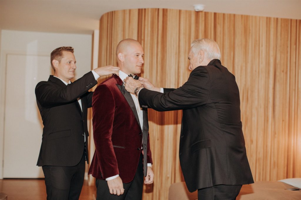 groom gets dressed in maroon velvet suit jacket