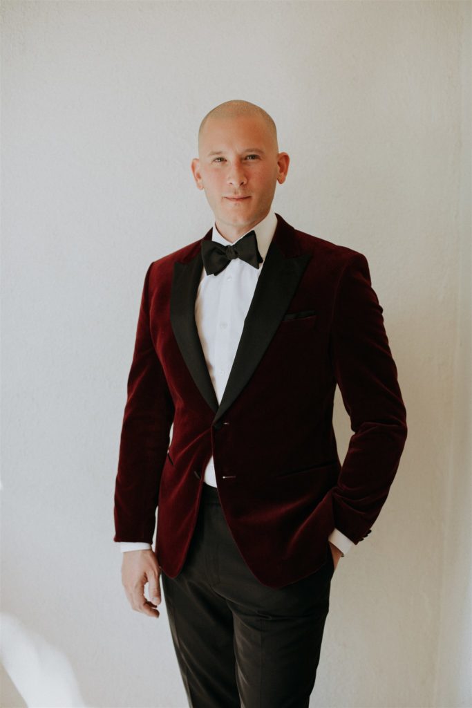 groom in maroon velvet suit jacket with black bowtie