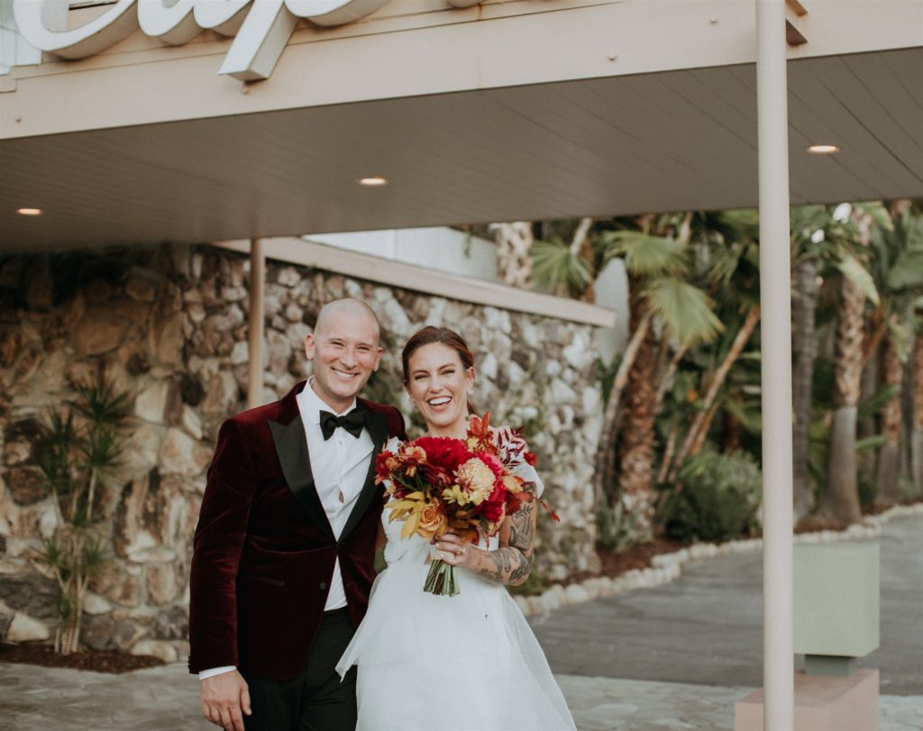 bride holding bright bridal bouquet with groom in maroon velvet suit for this mid-century wedding in Ojai