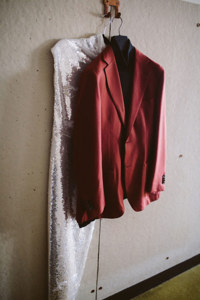 sparkly silver wedding dress and red groom suit jacket hang on wall