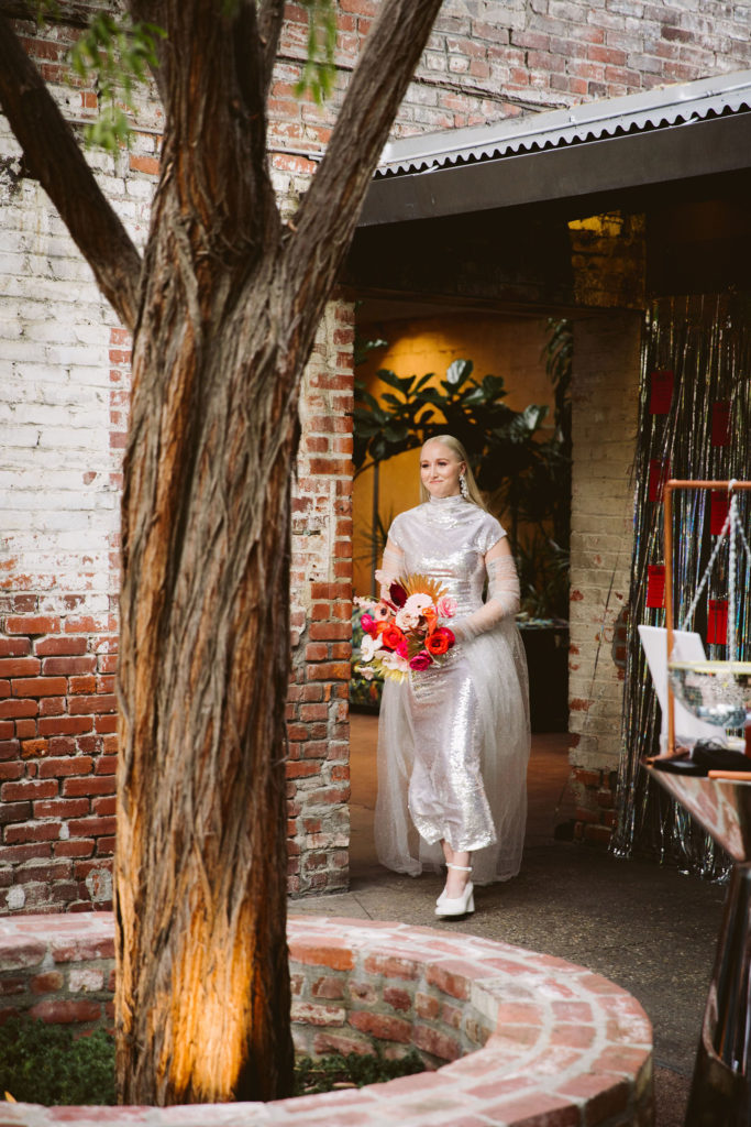 bride in silver wedding dress with pink and red bouquet walks down the aisle