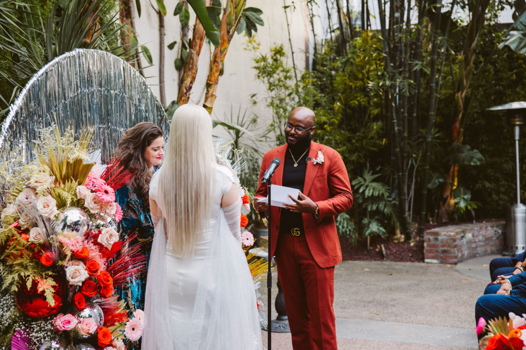 groom in red suit reads vows during wedding ceremony at Millwick in DTLA