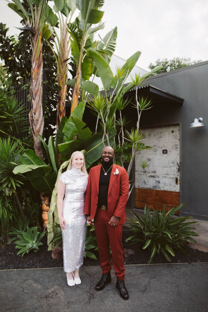 bride with long straight blonde hair wears silver wedding dress with groom in red suit stand for portraits at Millwick in DTLA