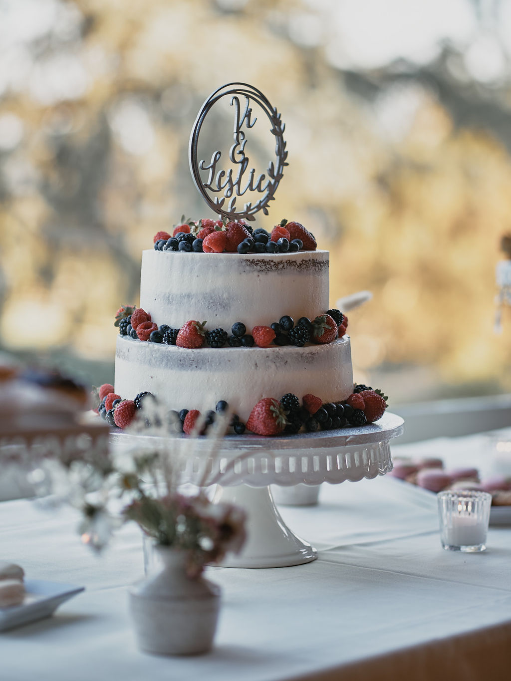 two tier naked wedding cake with fruit and silver cake topper