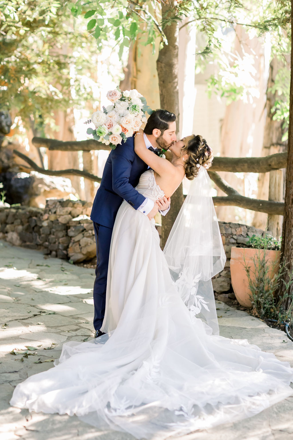 groom with paisley detail bowtie and blue tuxedo kisses bride in embellished chiffon strapless wedding dress at Calamigos Ranch