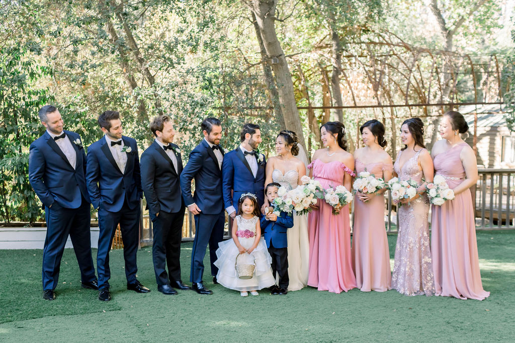 bride and groom stand with wedding party in blue tuxedo suits and mix matched blush pink dresses