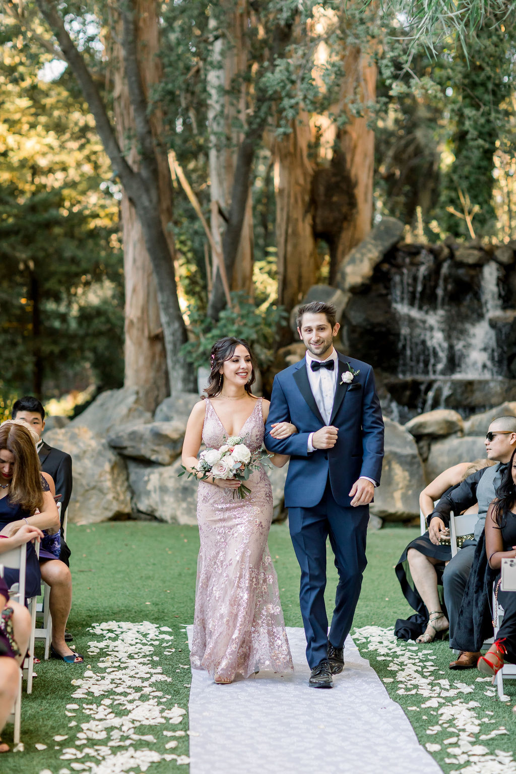 groomsman in blue suit walks with bridesmaid in blush pink dress