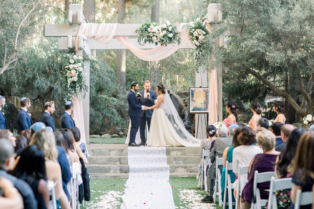 bride and groom hold hands during romantic and glamorous wedding ceremony at Calamigos Ranch