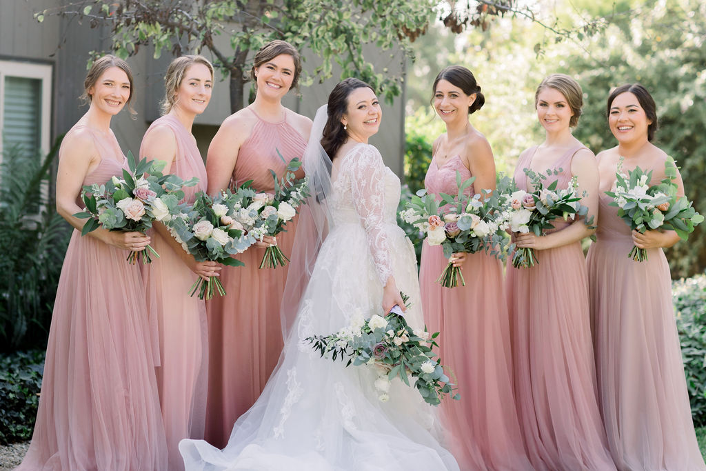bride in long sleeve wedding dress with bridesmaids in pink dresses holding romantic bouquets
