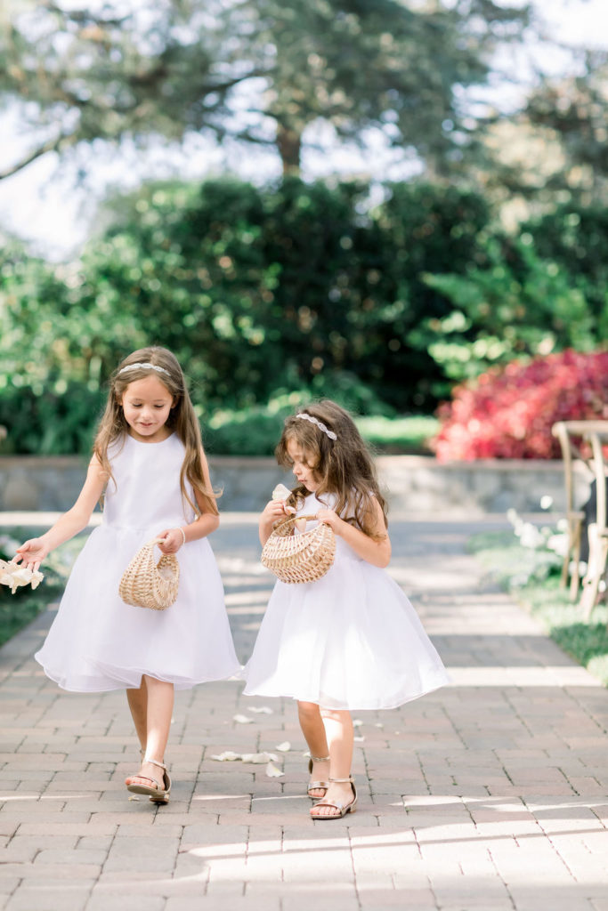 flower children wearing white dresses toss petals from small wicker baskets