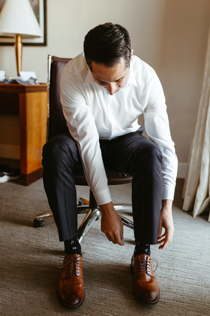 groom in navy suit putting on brown shoes