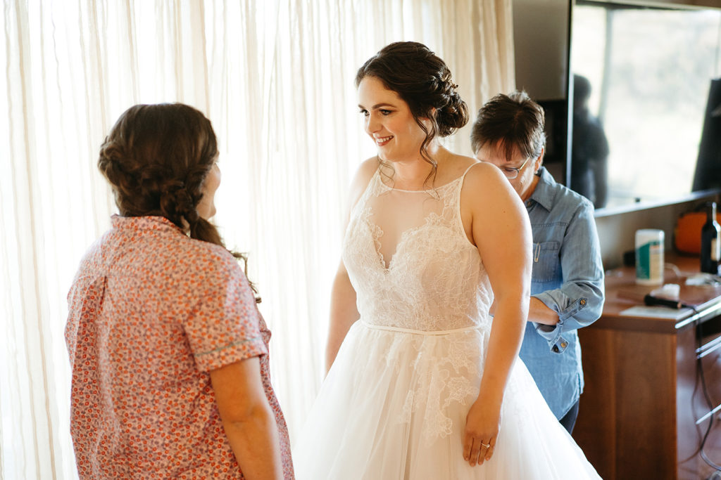 bride getting dressed in tiered ballgown wedding dress with lace detail on sweetheart neckline and champagne silk lining