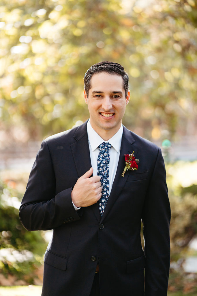 Outdoor wedding portrait shots at Temecula Creek Inn with groom in navy suit and floral tie and red boutonniere 