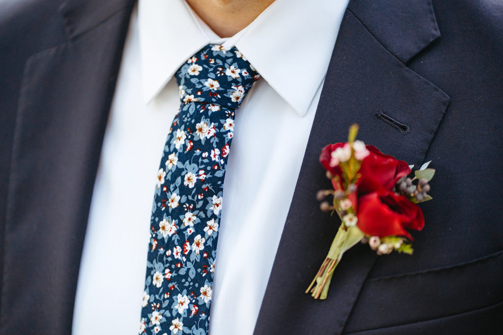 navy wedding suit with floral tie and red boutonniere 