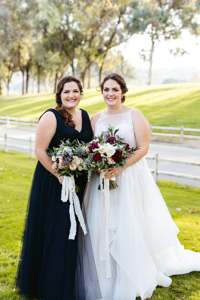 bride in tiered ballgown wedding dress stands with bridesmaid in navy blue dress with blue, white and red bouquets