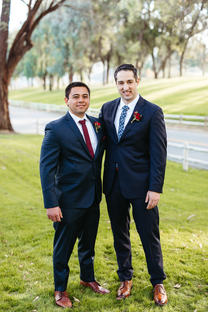 groom in navy suit and floral tie stands with groomsman in navy suit and red tie